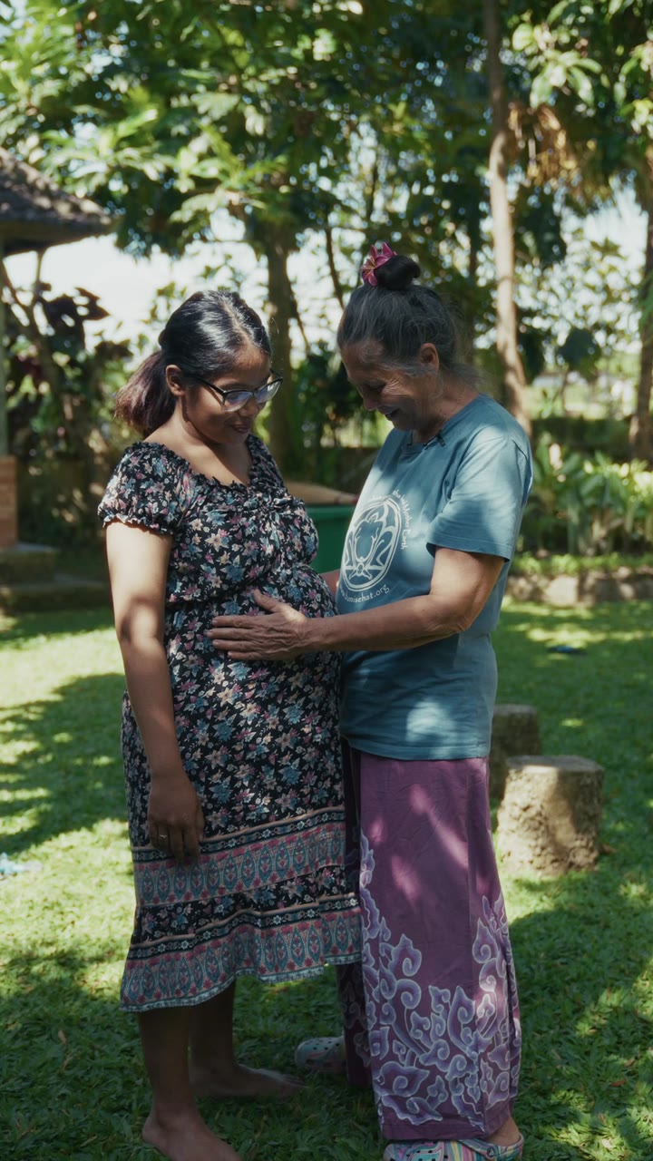 A birth worker’s hands on a pregnant woman’s belly, in the garden