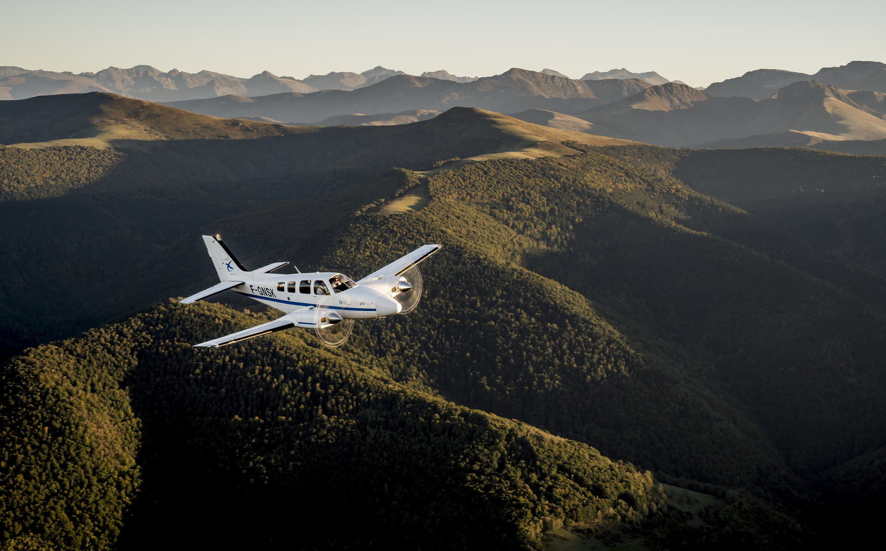 A twin-engine aircraft banking over forested ridges