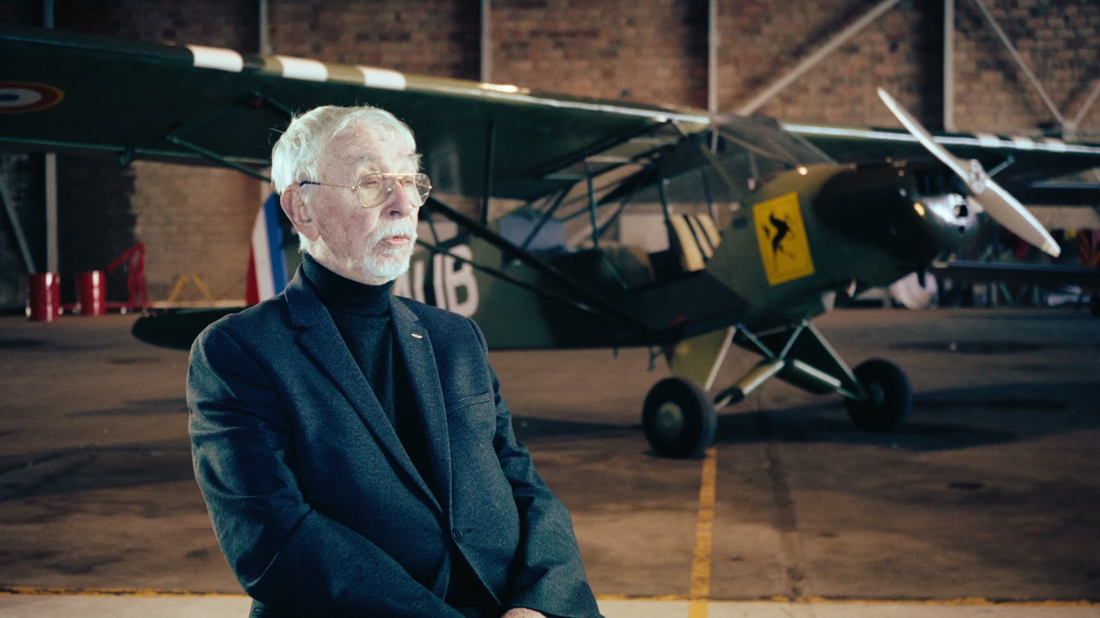 A veteran in front of the Piper in its hangar